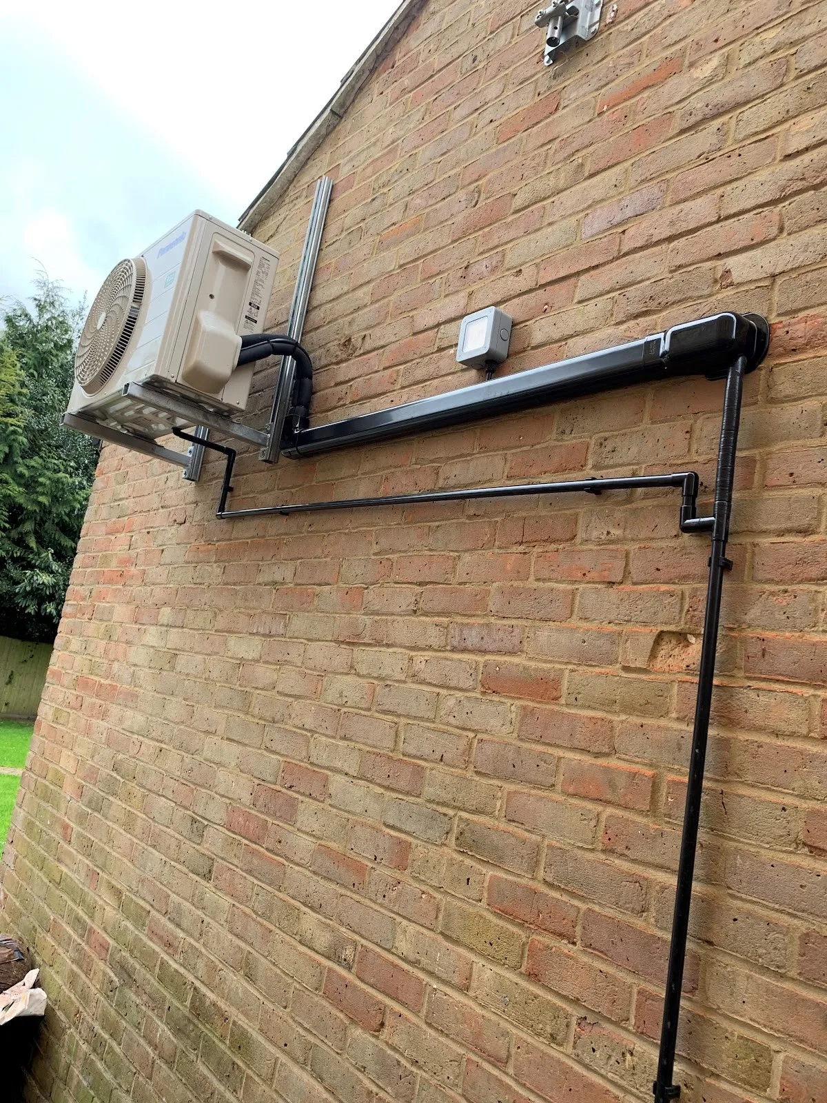 Outdoor unit on wall brackets. Pipework run in neat black trunking down the wall.